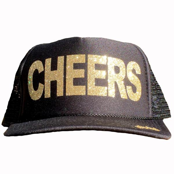 Cheers in glitter gold ink on the front panel of a black mesh trucker cap with an adjustable snapback