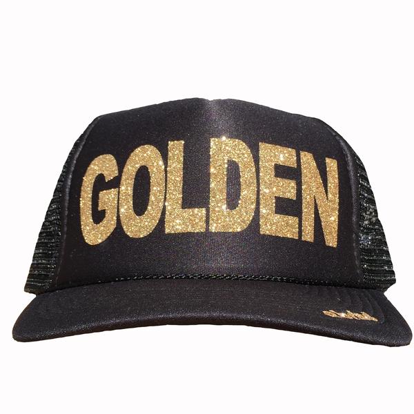 Golden in glitter gold ink on the front panel of a black mesh trucker cap with an adjustable snapback